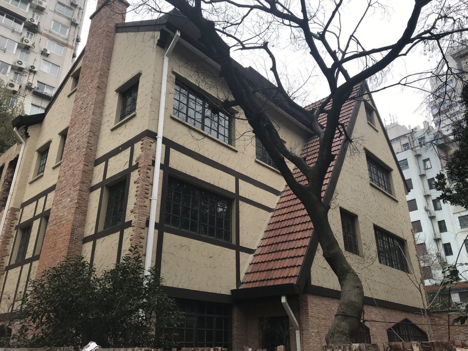 一栋三层老洋房的侧面，半木构外墙、红瓦斜顶，背后是现代高楼