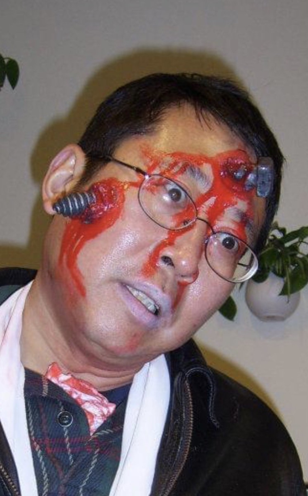 A man in glasses with Halloween make-up: fake blood across his face and plastic bugs stuck to his cheek and temple