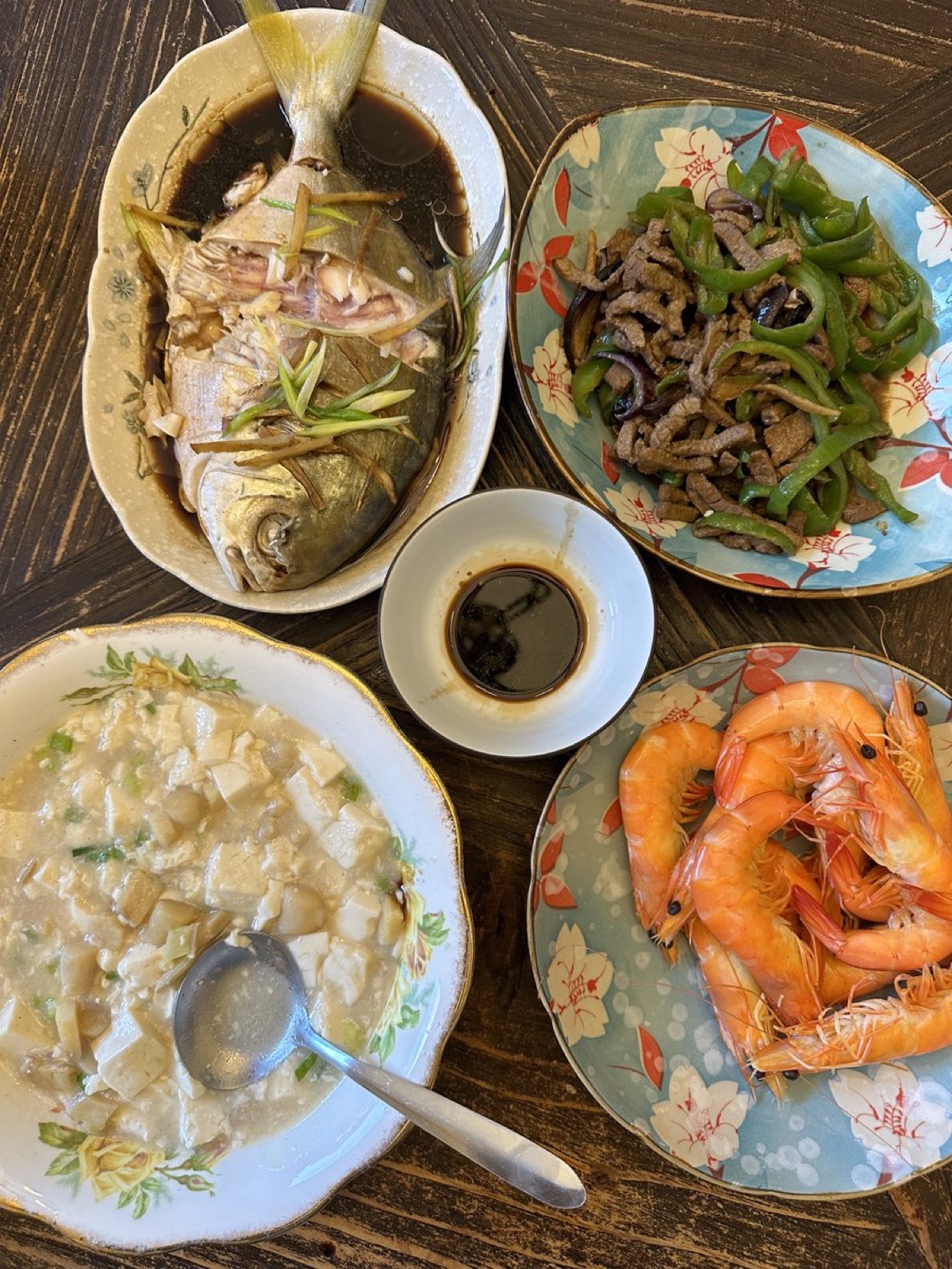 俯拍的家中餐桌：清蒸鲳鱼、青椒牛肉、白灼虾和一碗豆腐羹